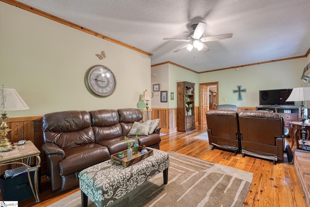 living area featuring wood finished floors, a textured ceiling, crown molding, a ceiling fan, and wainscoting