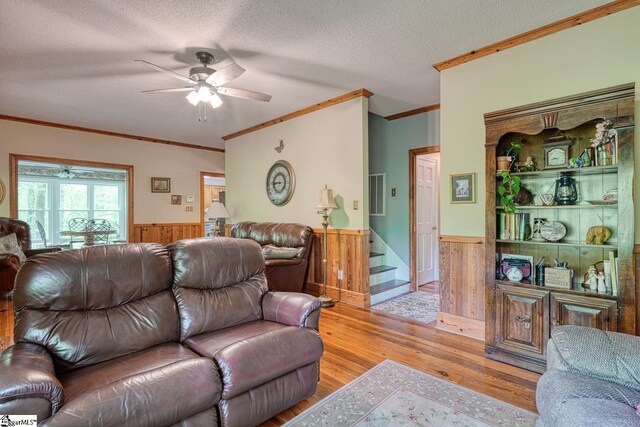 living area with crown molding, wood walls, a wainscoted wall, and a ceiling fan