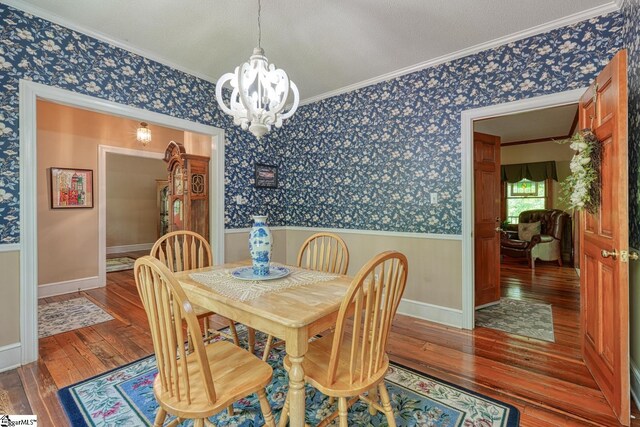 dining area with wood-type flooring, wallpapered walls, crown molding, wainscoting, and a chandelier