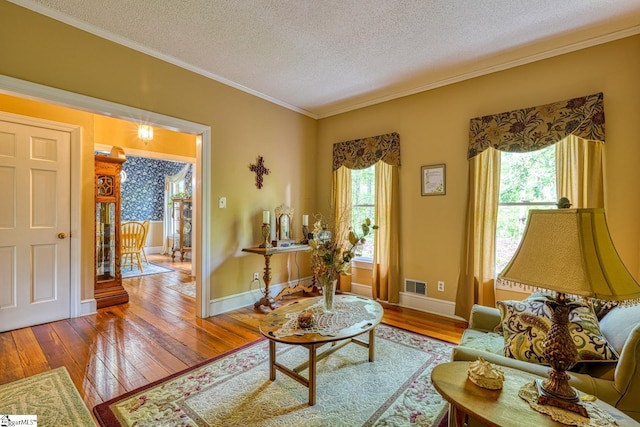 living room with hardwood / wood-style floors, ornamental molding, a textured ceiling, visible vents, and baseboards