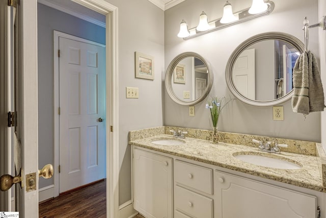 full bath featuring a sink, double vanity, ornamental molding, and wood finished floors