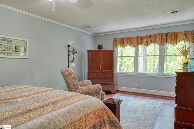 bedroom featuring wood finished floors, a textured ceiling, visible vents, crown molding, and baseboards