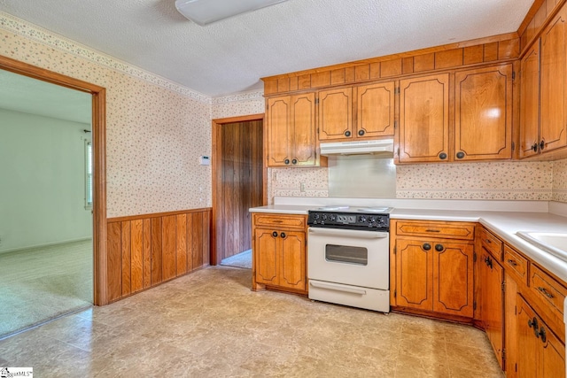 kitchen with brown cabinetry, under cabinet range hood, white range with electric cooktop, wainscoting, and wallpapered walls