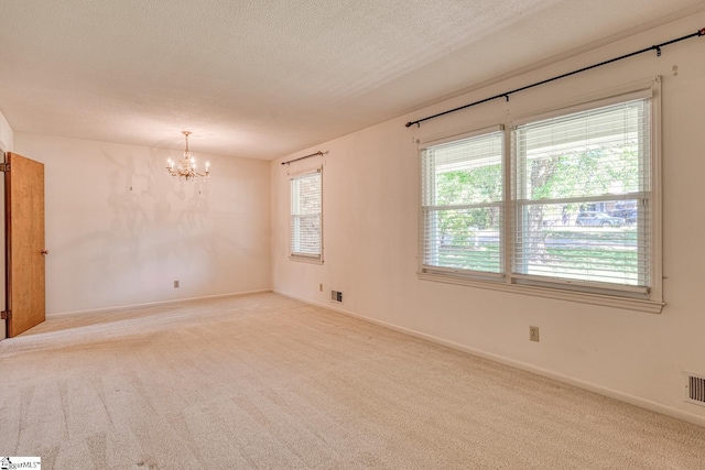 carpeted empty room with a chandelier, a textured ceiling, a wealth of natural light, and visible vents