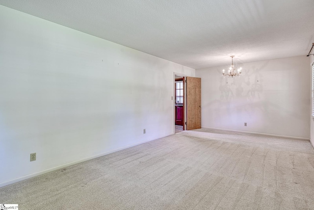 carpeted empty room featuring a textured ceiling, baseboards, and a notable chandelier
