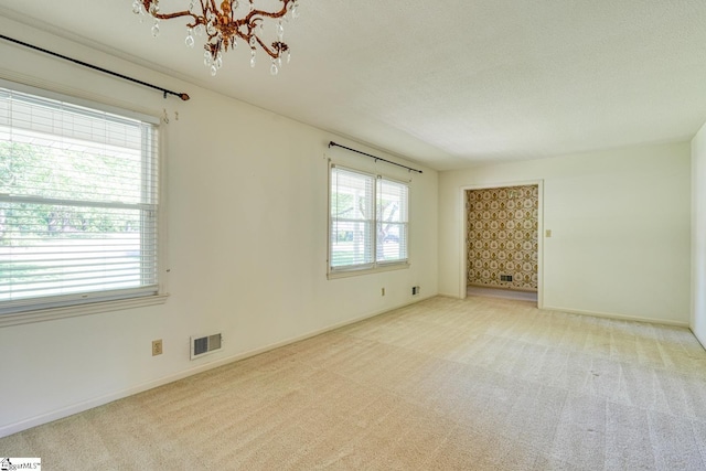 spare room with plenty of natural light, an inviting chandelier, visible vents, and carpet