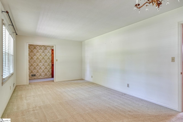 spare room featuring a textured ceiling, carpet flooring, a notable chandelier, and baseboards