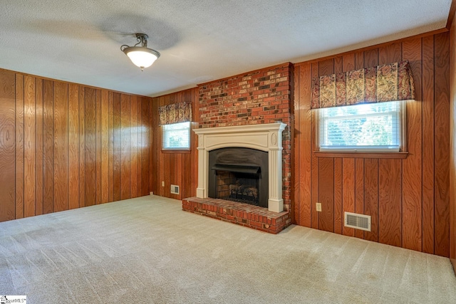 unfurnished living room with visible vents, wooden walls, a fireplace with raised hearth, and carpet floors