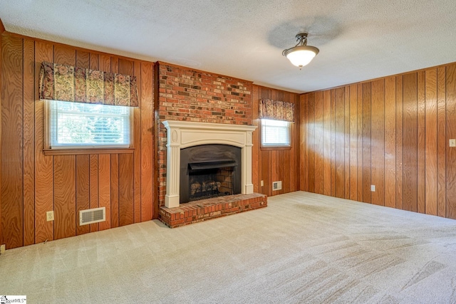unfurnished living room with carpet flooring, visible vents, a fireplace with raised hearth, and wooden walls