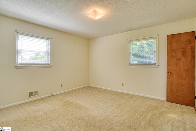 empty room with a textured ceiling, visible vents, baseboards, and light carpet