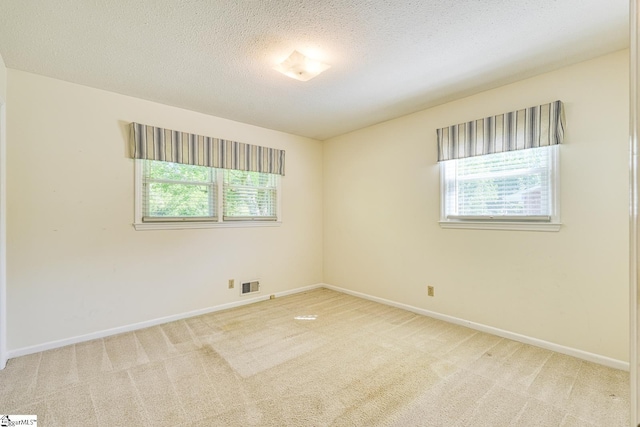 carpeted spare room featuring plenty of natural light, visible vents, and baseboards