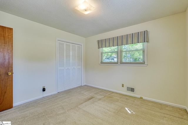 unfurnished bedroom featuring a closet, carpet floors, a textured ceiling, visible vents, and baseboards