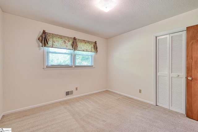 unfurnished bedroom with a closet, carpet floors, a textured ceiling, visible vents, and baseboards