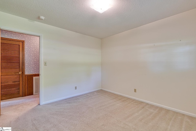 carpeted empty room with wainscoting, a textured ceiling, baseboards, and visible vents