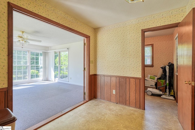 interior space featuring wallpapered walls, wainscoting, and ceiling fan