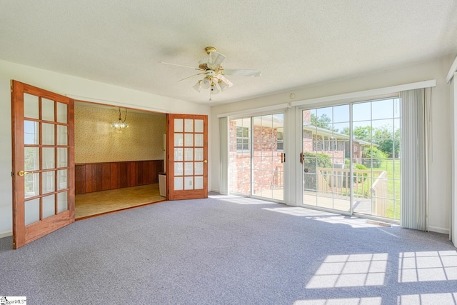 empty room featuring carpet, a textured ceiling, wooden walls, and ceiling fan with notable chandelier