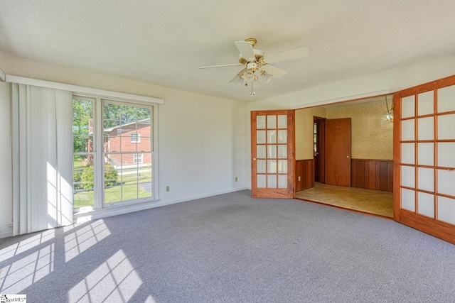 carpeted empty room featuring wood walls, baseboards, a wainscoted wall, and a ceiling fan