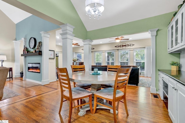 6 Shallow Creek Ct, Fountain Inn, SC 29644 - dining area featuring ceiling fan with notable chandelier, decorative columns, high vaulted ceiling, light wood-style flooring, and a glass covered fireplace