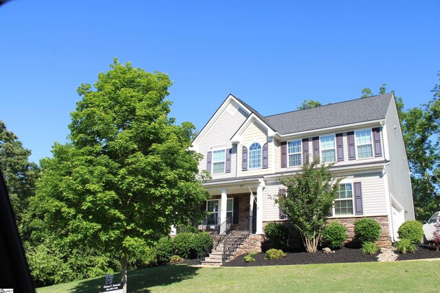 view of front of home with stairway, a porch, stone siding, and a front yard
