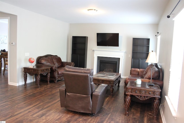 living room featuring baseboards, dark wood-type flooring, and a glass covered fireplace