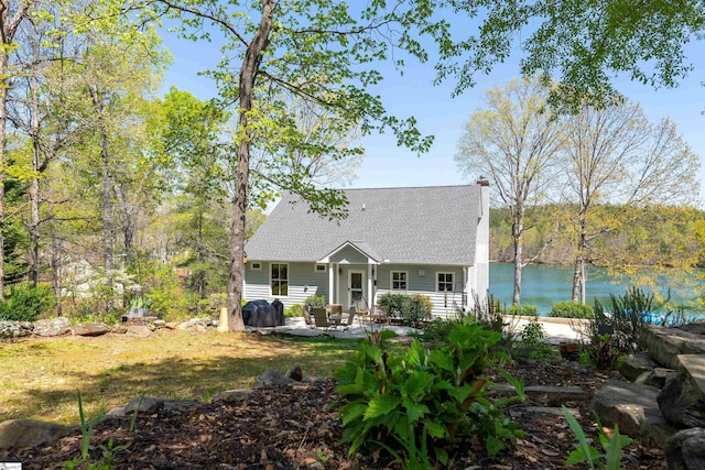 back of property featuring a patio, a shingled roof, a water view, and a chimney