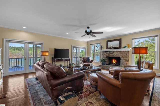 living room with a stone fireplace, a ceiling fan, crown molding, french doors, and wood finished floors