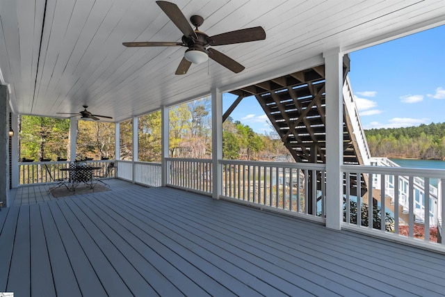 wooden terrace with stairs, ceiling fan, outdoor dining area, and a water view