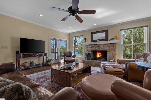 living area featuring ornamental molding, healthy amount of natural light, wood finished floors, a ceiling fan, and a stone fireplace