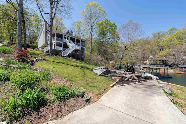 view of green lawn with a sunroom, stairs, and a dock