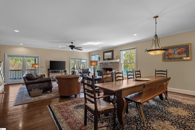 dining space with plenty of natural light, a stone fireplace, ornamental molding, a ceiling fan, and dark wood finished floors