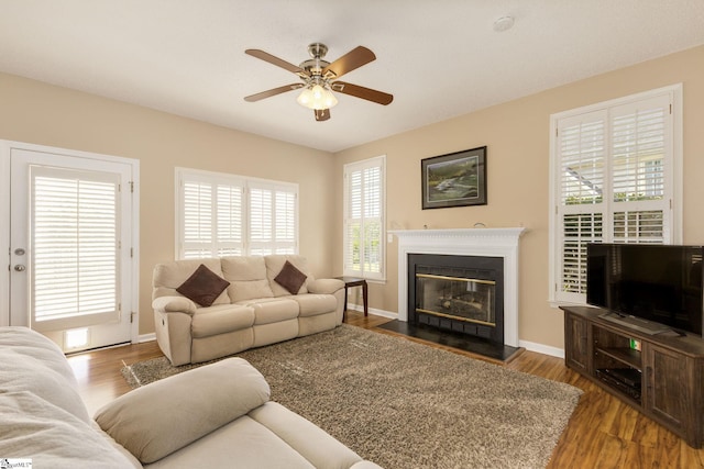 living room featuring ceiling fan, wood finished floors, a glass covered fireplace, and baseboards