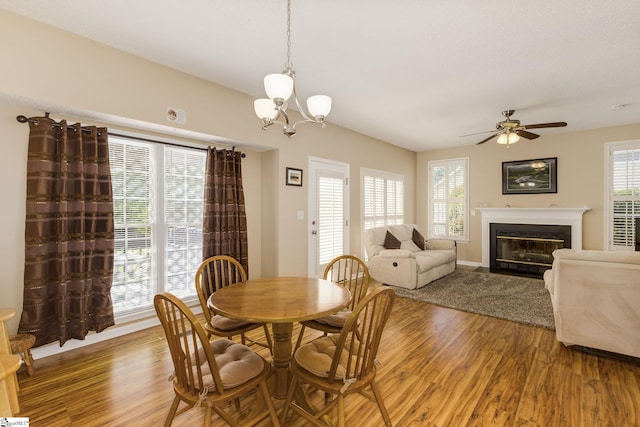 dining space with light wood finished floors, a fireplace with flush hearth, ceiling fan, and a chandelier