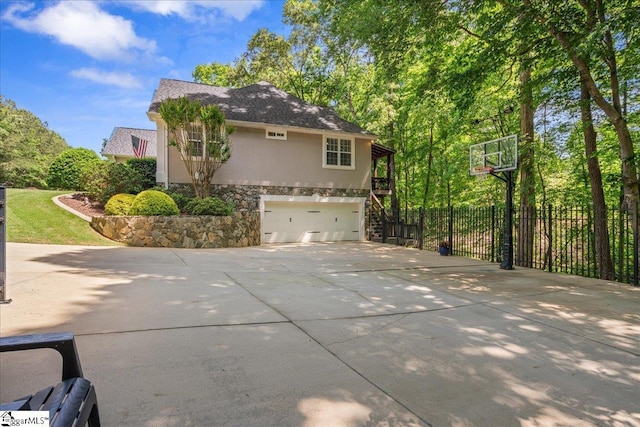 view of side of home featuring stone siding, stucco siding, driveway, a garage, and fence