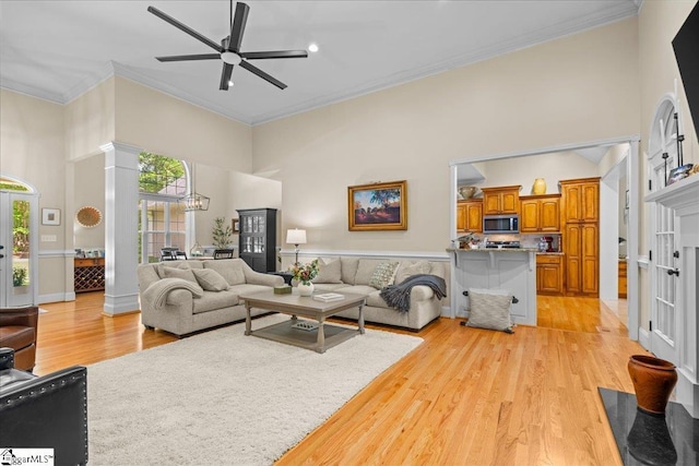 living area with a high ceiling, plenty of natural light, ornamental molding, a ceiling fan, and light wood-type flooring