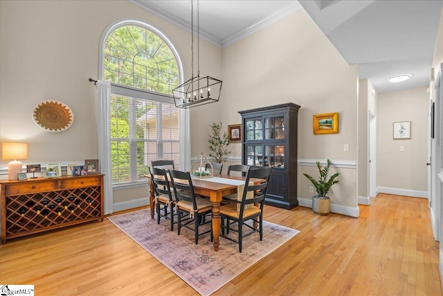 dining room with light wood-style flooring, a chandelier, baseboards, ornamental molding, and a towering ceiling