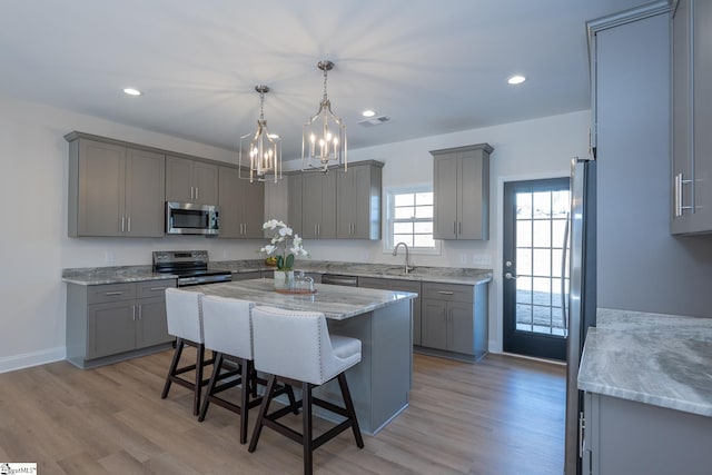 kitchen with appliances with stainless steel finishes, gray cabinets, a sink, a breakfast bar, and recessed lighting