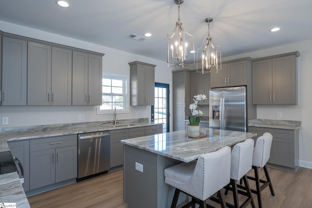 kitchen with stainless steel appliances, a sink, gray cabinets, a chandelier, and a center island