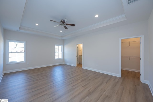 unfurnished bedroom featuring a raised ceiling, a walk in closet, wood finished floors, recessed lighting, and ornamental molding