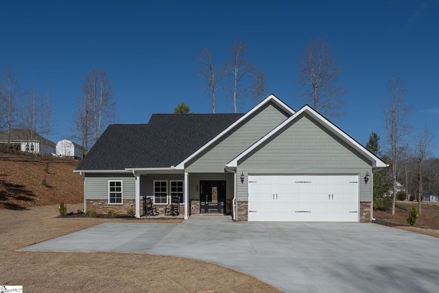 view of front of house featuring an attached garage, stone siding, a porch, and driveway