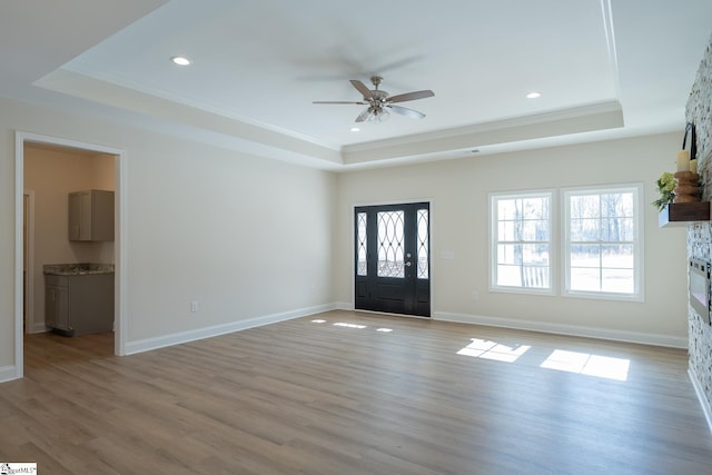 foyer entrance with a raised ceiling, crown molding, ceiling fan, light wood finished floors, and baseboards
