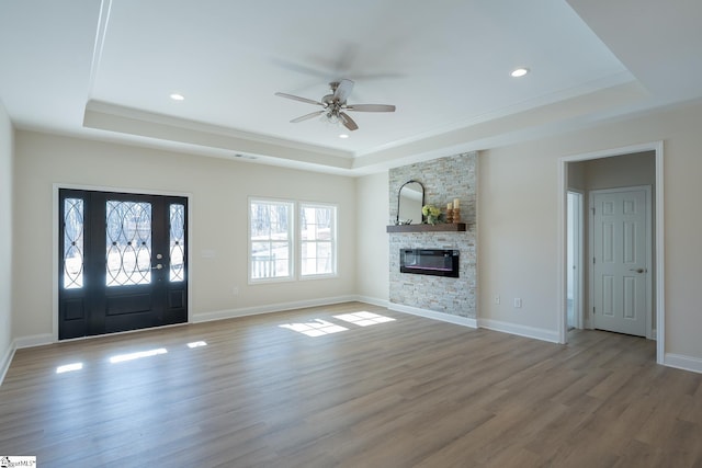 unfurnished living room featuring a tray ceiling, ceiling fan, a fireplace, crown molding, and recessed lighting