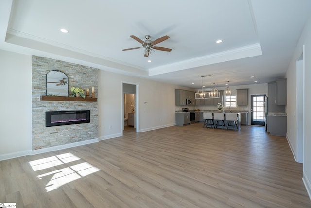 unfurnished living room featuring a tray ceiling, ceiling fan, a fireplace, crown molding, and light wood-style floors