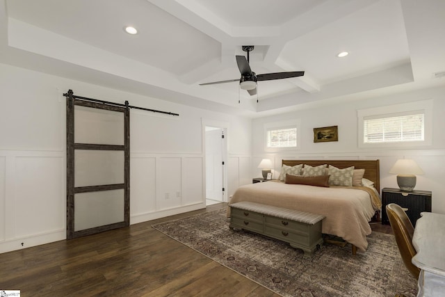 bedroom with a barn door, a decorative wall, dark wood-style floors, coffered ceiling, and a wainscoted wall
