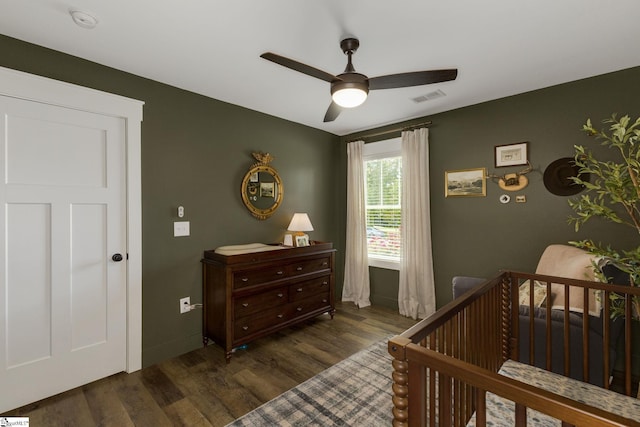 bedroom featuring dark wood finished floors, a nursery area, ceiling fan, and baseboards