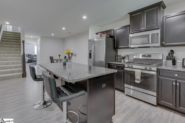 321 Aldworth Ln, Fountain Inn, SC 29644 - kitchen featuring stainless steel appliances, a kitchen island, light wood finished floors, a breakfast bar area, and light stone countertops