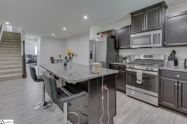 321 Aldworth Ln, Fountain Inn, SC 29644 - kitchen featuring stainless steel appliances, a kitchen island, light wood finished floors, a breakfast bar area, and light stone counters