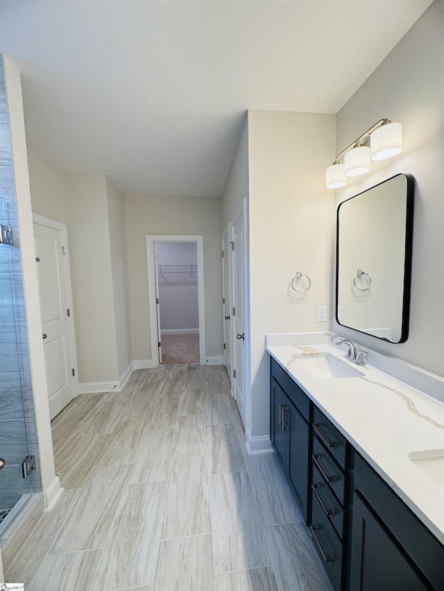 bathroom with double vanity, a stall shower, a walk in closet, and baseboards