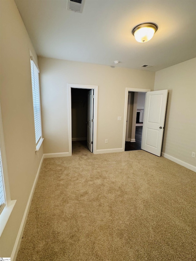 unfurnished bedroom featuring carpet flooring, baseboards, a walk in closet, and a closet