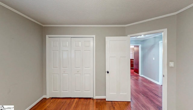 unfurnished bedroom with wood finished floors, baseboards, a closet, crown molding, and a textured ceiling