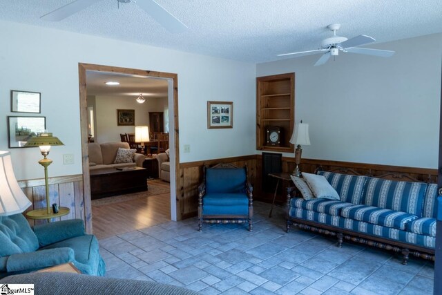 living area with a ceiling fan, a wainscoted wall, a textured ceiling, and wooden walls